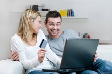 Young smiling couple making shopping online with credit card at homeの写真素材