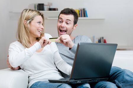 Young couple contend for a credit card for internet shopping with fun at homeの写真素材