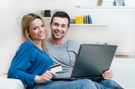 Smiling young couple making shopping online with credit card and laptop at homeの写真素材
