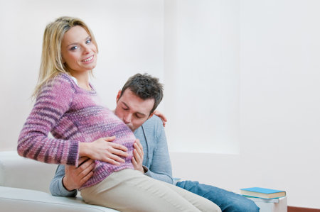 Happy father give a sweet kiss to the mother's bump of their new child