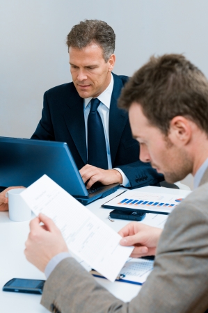 Mature businessman typing on his laptop during a business meeting in officeの写真素材