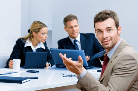 Smiling happy businessman with colleaugues in the background at meeting in the officeの写真素材
