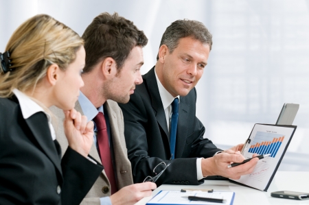 Satisfied senior businessman showing growing chart at his happy colleagues in modern officeの写真素材