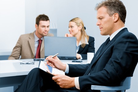Pensive absorbed mature businessman working on growing chart with colleagues in backgroundの写真素材