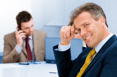 Smiling senior businessman looking at camera with satisfaction and colleague in the backgroundの写真素材