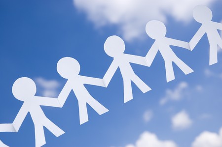 Paper man chain on blue sky with white clouds. Symbol of unity, brotherhood and teamwork.の写真素材
