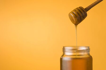 Honey falling from a dipper into a jar on orange background. Space for textの写真素材