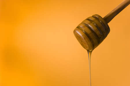 Detail of honey falling from a dipper. Orange background. Space for textの写真素材