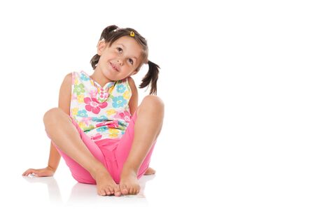 Smiling little girl imagining and sitting on floor isolated on white backgroundの写真素材
