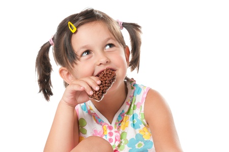 Little girl eating cereal bar for snack isolated on white backgroundの写真素材