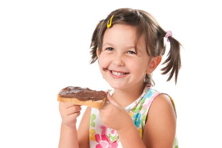 Happy smiling little girl biting a slice of bread with chocolate spread for snack isolated on white backgroundの写真素材