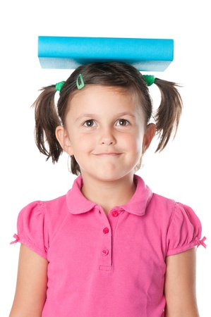 Smiling satisfied little girl holding a book on her head isolated on white backgroundの写真素材