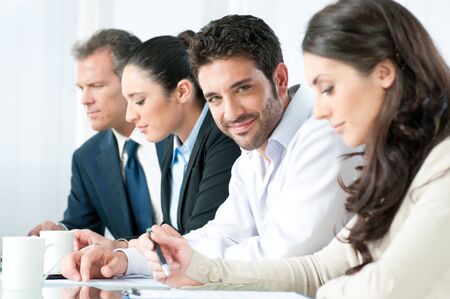 Smiling proud business man looking at camera with satisfaction and working colleagues in officeの写真素材