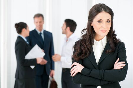 Smiling confident business woman looking at camera with her colleagues in background at officeの写真素材