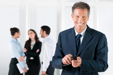 Happy smiling mature businessman receveing positive news on his smart phone at officeの写真素材