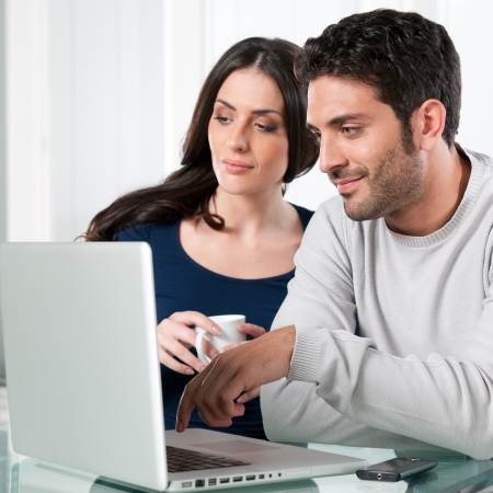 Smiling beautiful young couple surfing the net with laptop at homeの写真素材