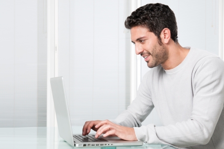 Happy smiling young man working and typing on laptop at homeの写真素材
