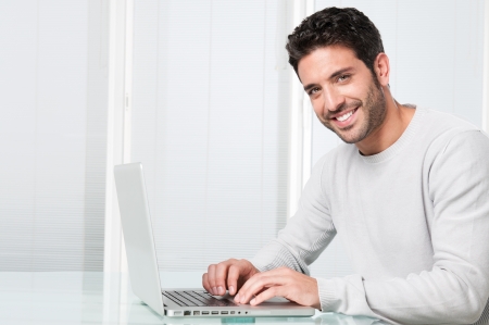 Happy satisfied young man working on laptop and looking at cameraの写真素材