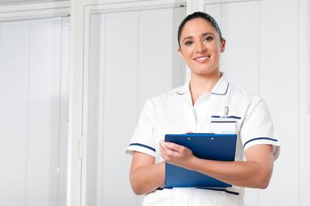 Smiling young brunette female nurse looking at camera at hospitalの写真素材