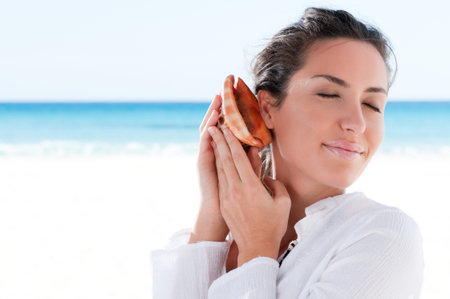 Beautiful young woman holding a Shell and dreaming a summer vacation