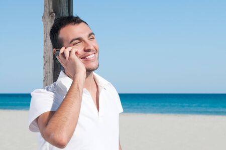 Happy smiling young man talking on mobile at summer beachの写真素材