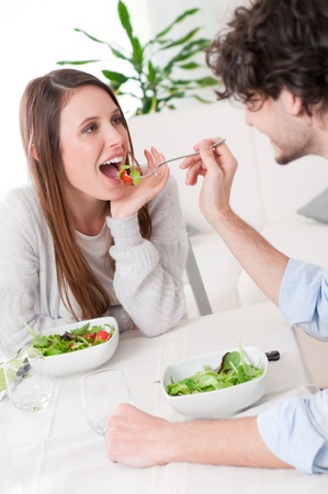 Young man feeding his girlfriend with fresh salad at homeの写真素材