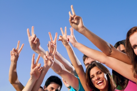 Happy group of young friends showing victory hand sign over blue skyの写真素材