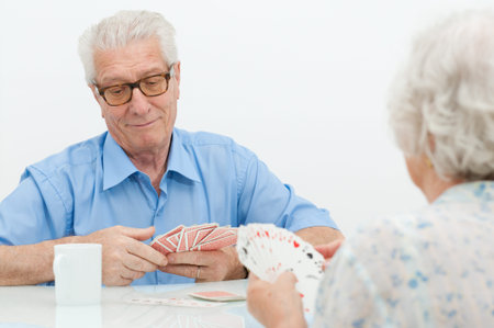 Happy old couple playing together with  cards at homeの写真素材