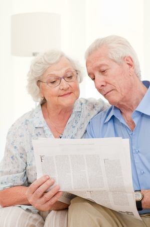 Happy relaxing senior couple reading newspaper together at homeの写真素材