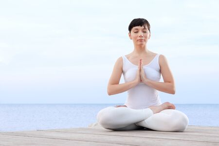 Healthy young woman meditating in yoga lotus pose at seaの写真素材