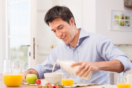 Happy Young Man Pouring Milk Into Bowl For Breakfast