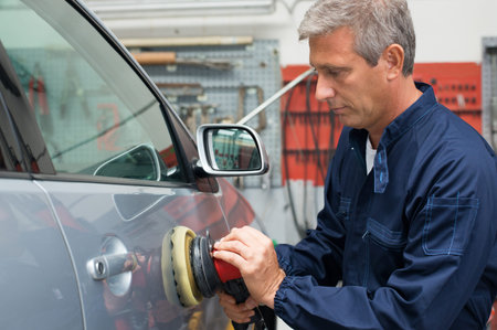 Portrait Of Mature Auto Mechanic Polishing Car At Workshop