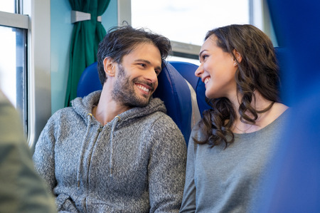 Closeup of happy young couple traveling by train together. They are looking at each other while smiling and enjoy the trip. They are sit on blue seats in a train's coach.の写真素材