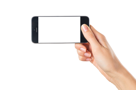 Closeup shot of a woman showing modern mobile phone isolated on white background. Girl holding a smartphone with white screen in horizontal. Young woman's hand showing an horizontal cellphone.の写真素材
