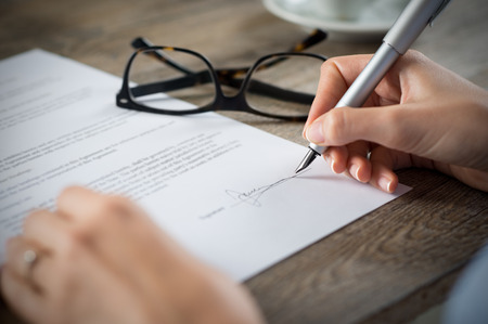 Closeup shot of a woman signing a form. She's writing on a financial contract. Shallow depth of field with focus on tip of the pen.の写真素材