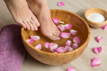 Closeup shot of a woman feet dipped in water with petals in a wooden bowl. Beautiful female feet at spa salon on pedicure procedure. Shallow depth of field with focus on feet.の写真素材