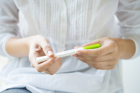 Closeup shot of a woman looking at pregnancy test. She's is checking her pregnancy exam. Detail hands of a girl holding pregnancy test. Shallow depth of field with focus on pregnancy test.の写真素材