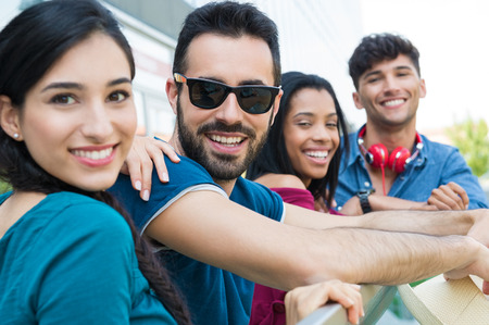 Closeup shot of young friends leaning on railing. Happy smiling girls and guys looking at camera. Happy young couple in a summer day.の写真素材