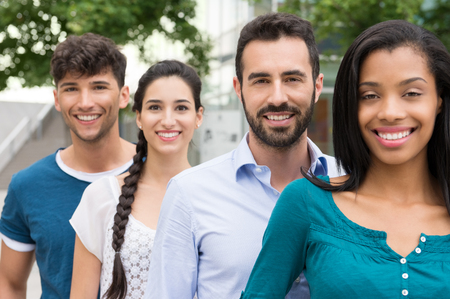 Closeup shot of young friends standing in a row outdoor. Happy group of men and women smiling and looking at camera. Happy young friends outside.