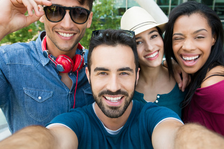 Closeup shot of young friends take a selfie. Happy smiling girls and guys photographing self. Laughing young women and men taking a photo and looking at camera.の写真素材