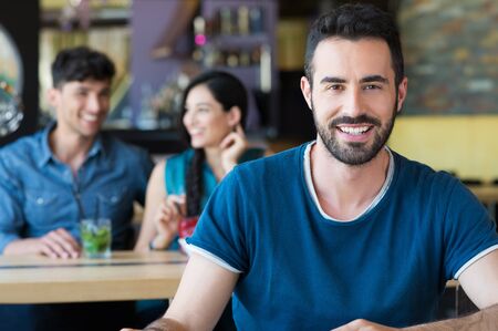 Closeup shot of young man looking at camera. Handsome guy smiling at coffee bar. Portrait of happy young man in casual sitting at a table in a bar.の写真素材