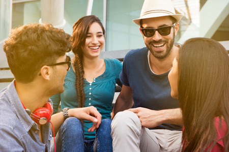 Portraits of young happy friends smiling and sitting on staircase having fun. Women and men laughing together outdoor in a summer day. Smiling girls and guys having fun sitting on staircase.の写真素材