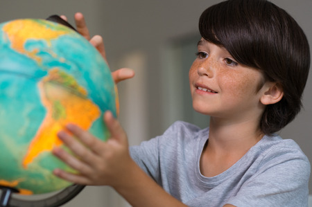 Closeup of little boy learning about the world using globe of earth. Male child studying globe at school. Cute boy looking at globe of earth.の写真素材