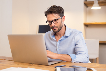 Young casual office worker working on laptop. Young businessman typing on laptop computer at office. Young man working absorbed on laptop at work place.