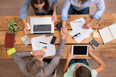 High angle view of businesspeople shaking hands and closing a deal. Successful business teamwork working at the office. Business partners sitting at table and planning work.