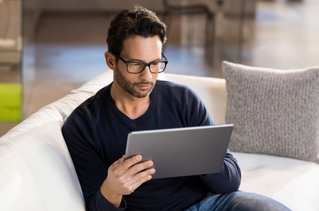 Portrait of a serious man wearing eyeglasses working on digital tablet at home.の写真素材