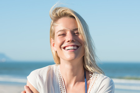 Portrait of a young cheerful woman smiling at the beach. Young blonde enjoying on a bright sunny day at the beach. Portrait of happy girl laughing and looking at camera.の写真素材