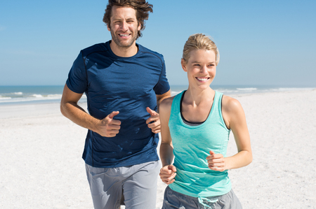 Couple exercising at beach. Trainer training athlete for fitness. Athletics jogging in summer sport shorts enjoying the sun.