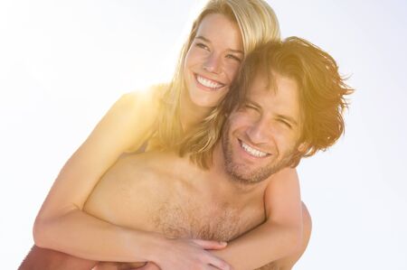 Young couple at beach enjoying summer. Boyfriend piggybacking his girlfriend at beach during honeymoon. Happy young joyful couple having fun in beach.の写真素材