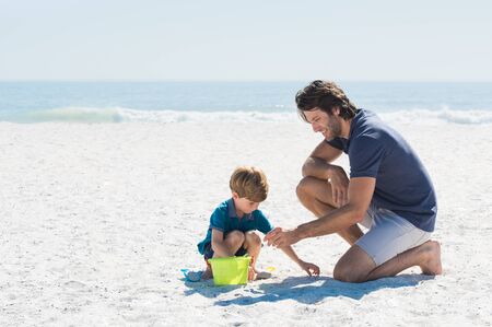 Father and son playing with toys at beach. Family of father and son enjoying summer vacation at beach. Father helping son fill basket with sand.の写真素材